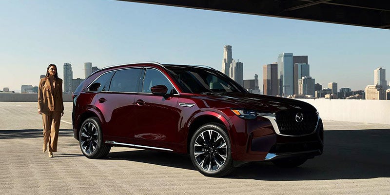 Dark red SUV parked on a rooftop, with a woman in a brown suit walking away from it
