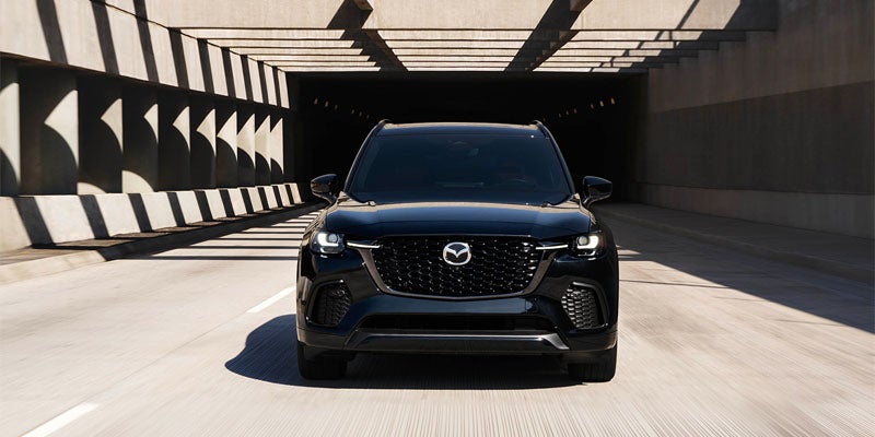 Front view of a dark Mazda SUV driving out of a concrete tunnel with geometric shadow patterns.
