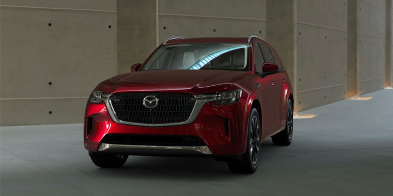 Red Mazda CX-90 SUV parked front-on in a modern concrete interior with a light-colored floor.