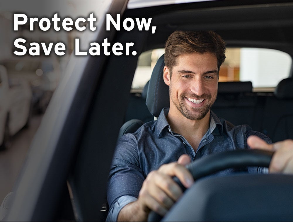 Smiling man driving a car, hands on the wheel, with text: Protect Now, Save Later.